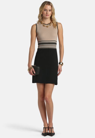 Kötött ruha bézs felsőrésszel fekete csíkokkal, testhezálló fekete szoknyával és elegáns sziluettel. Kiegészítve karkötővel és kézitáskával.