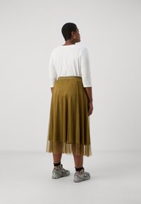 Hvit topp med trekvart ermer som er kombinert med en sennepsfarget plissékjole. Kjolen har en transparent finish og har en glatt livlinje. Sølvfargede joggesko fullfører antrekket.