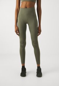 Olivgrüne, hochgeschnittene Leggings aus dehnbarem Stoff, mit einem körperbetonten Design und einem kleinen Logo an der Seite. Geeignet für Sportbekleidung.