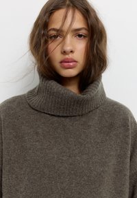 Dunkelbrauner, gerippter Rollkragensweater aus weichem, strukturiertem Stoff, mit lockerer Passform und hohem Kragen. Keine Muster oder Akzente sichtbar.