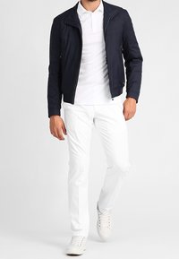 Námořnická lehká bomber bunda se zipem, v kombinaci s bílým polo tričkem a slim-fit bílými kalhotami. Dokončeno bílými teniskami.