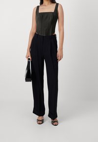 Pantalons noirs cintrés à jambe large, associés à un corset ajusté en satin vert foncé avec décolleté carré et plis subtils.