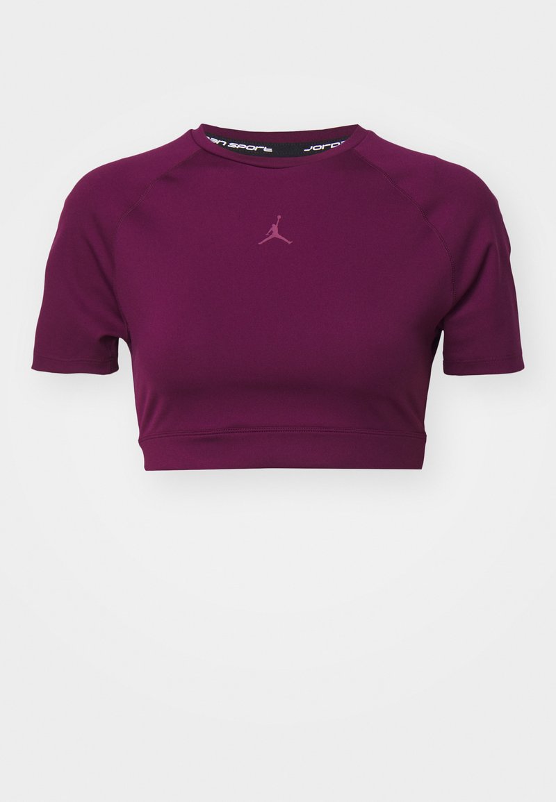 Kurzärmliges, cropped sportliches Oberteil aus einfarbigem, tiefviolettem Stoff, mit einem kleinen, hellvioletten Logo auf der Brust und einem schwarzen Innenkragen.