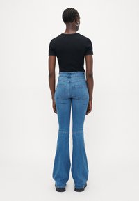 Camisa negra de manga corta combinada con vaqueros de mezclilla de tiro alto y acampanados. Los vaqueros tienen dos bolsillos traseros y una textura azul suave.