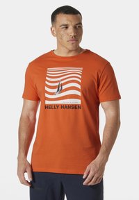 Oranžové bavlněné tričko s grafikou lodi obklopenou vlnitými čarami a textem "HELly Hansen" v tučném černém písmu.