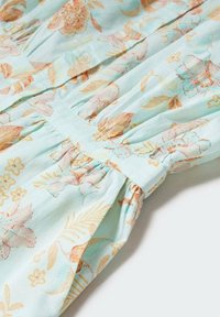 Tkanina w jasnoniebieskim kolorze, w kwiatowy wzór, z marszczoną teksturą i detalem w postaci guzika. Ozdobiona brzoskwiniowymi i żółtymi kwiatami, tworzy delikatny, naturalny wygląd.