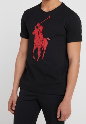 Homme portant un t-shirt noir avec un grand motif rouge représentant un joueur de polo à cheval brandissant un maillet à l'avant.