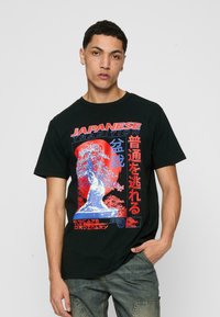 Juodas medvilnės marškinėliai su raudonu ir mėlynu grafiniu spaudiniu, kuriame yra japonų tekstas ir medžio dizainas. Standartinio silueto, su trumpomis rankovėmis.