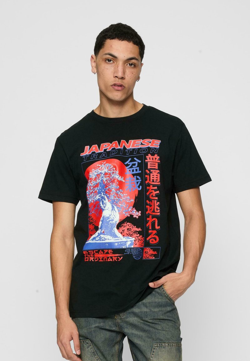 Juodas medvilnės marškinėliai su raudonu ir mėlynu grafiniu spaudiniu, kuriame yra japonų tekstas ir medžio dizainas. Standartinio silueto, su trumpomis rankovėmis.