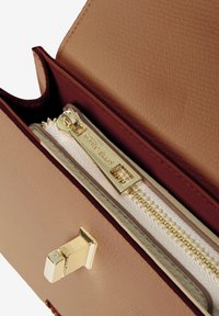 Portafoglio in pelle beige con un accento bordeaux, dotato di una cerniera e hardware dorati, e di un vano interno con una tasca con cerniera.