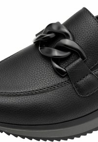 Chaussure en cuir noir avec une surface texturée, ornée d'une chaîne noire brillante sur le devant et dotée d'une semelle robuste pour une meilleure traction.