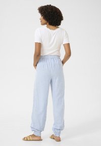 Bela rebrasta majica s kratkimi rokavi, svetlo modri in beli prugasti hlače z elastičnim pasom, z zakroženimi gležnji, v kombinaciji s svetlo bež sandali.