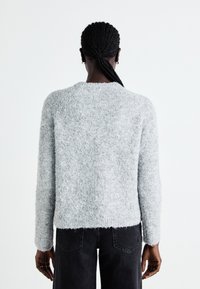 Pull en laine grise flou avec un col rond et des manches longues, doté d'une finition tricotée texturée. Associé à un jean noir taille haute.