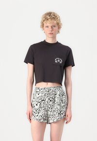 Cropped black cotton t-shirt with a front pocket, paired with white shorts featuring a black abstract pattern and elastic waistband.