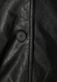 Czarny skórzany ubiór o gładkiej fakturze, z wyraźnym detalem guzikowym i widocznym przeszyciem wzdłuż szwu.