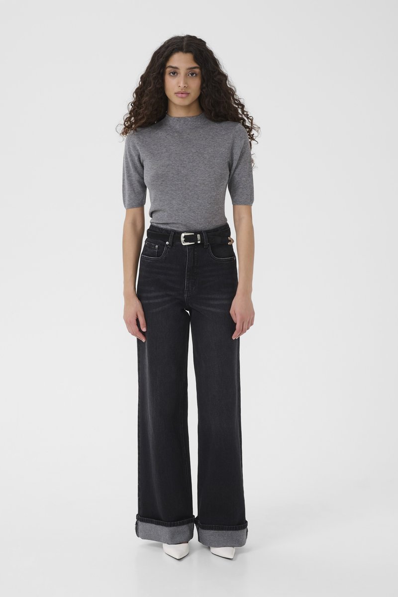 Top grigio in maglia con maniche corte abbinato a jeans di denim scuro a gamba larga e vita alta con orli risvoltati. Décolleté bianchi con punta appuntita.