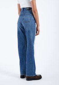 Jeans de mezclilla azul de pierna ancha con una cintura alta, con un bolsillo trasero de parche, detalles cosidos y un parche de cuero con el logo en la cintura.