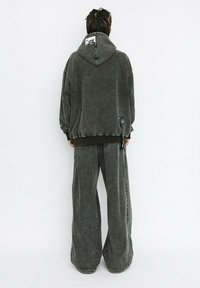 Sudadera gris de gran tamaño con capucha y etiqueta en la parte posterior, combinada con pantalones de mezclilla grises de pierna ancha. La tela tiene una textura ligeramente desgastada.