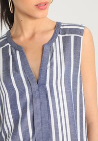 Camisa sin mangas con rayas verticales en azul y blanco, hecha de una tela ligera con una textura sutil y un escote con muesca.