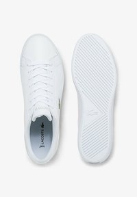 Baskets blanches Lacoste avec un dessus en synthétique lisse, bout arrondi, fermeture à lacets, accent logo vert et semelle en caoutchouc texturé.