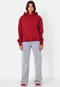 Hoodie bordeaux avec une poche avant et des boutons au col, associé à un jean évasé bleu clair et des baskets rouges.