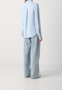 Camicia azzurro chiaro a maniche lunghe con righe sottili, orlo curvo e polsini con bottone, abbinata a pantaloni in denim larghi e di un blu chiaro.