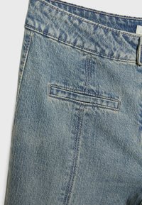 Jeans de mezclilla azul claro con un acabado texturizado descolorido, que cuentan con un bolsillo trasero, costuras visibles y un diseño de cinturilla estándar.