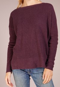 Lila ribbad stickad tröja med en bred halsringning och långa ärmar, tillsammans med blå denimjeans. Har en avslappnad passform och mjuk textur.