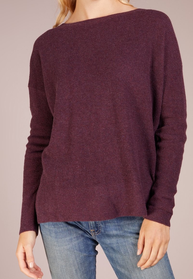 Lila ribbad stickad tröja med en bred halsringning och långa ärmar, tillsammans med blå denimjeans. Har en avslappnad passform och mjuk textur.