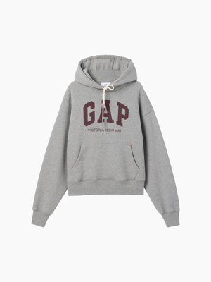 Sweat à capuche gris avec texte "GAP" bordeaux et texte plus petit "Victoria Beckham" en dessous, avec poche kangourou à l'avant et capuche avec cordon.
