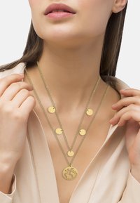 Gouden gelaagde ketting met drie kettingen en ronde bedels, waaronder een wereldbol hanger. Het ontwerp is strak met een gepolijste afwerking.