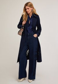 Abrigo navy con recortes detallados, combinado con unos vaqueros de pierna ancha con bordado floral y unos tacones beige de punta.