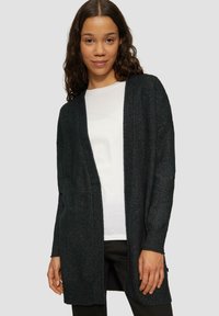 Schwarze Strickjacke mit langen Ärmeln, offener Vorderseite und gerippten Bündchen. Weiche Textur mit einem subtilen Schimmer, getragen über einem weißen Hemd.