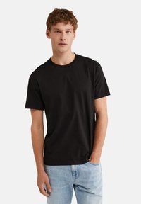 Camiseta de algodón negra con cuello redondo, mangas cortas, textura suave y ajuste relajado, combinada con unos vaqueros de color azul claro.