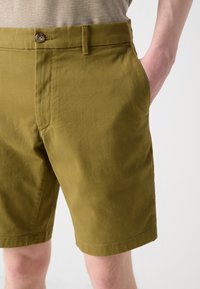 Olivengrønne bomullsshorts med flat front, enkel knappelukking, skrå sidelommer og pent søm langs kanten.