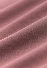 Artimos plano minkštos, tekstūruotos mauve spalvos medžiagos su smulkiu mezgimo raštu ir švelniais raukšlėmis, sudarančiomis paralelines bangas.