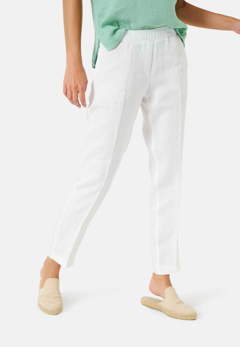 Bílé lněné kalhoty s tapered střihem a elastickým pasem, doplněné béžovými nazouvacími botami. Outfit zahrnuje světle zelený top.