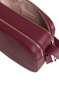 Borsa in pelle bordeaux con finitura testurizzata, due chiusure a cerniera dorate e un interno beige con un'etichetta che recita "Coccinelle Pelle Italiana Autentica."