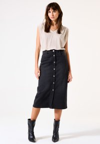 Schwarzer Jeansrock mit Knopfverschluss vorne, tailliertem Bund und knielangem Saum. Kombiniert mit einem hellbeigen ärmellosen Oberteil und schwarzen Knöchelstiefeln.