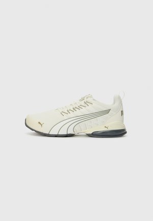 Witte en beige Puma sportschoen met zwarte zoolaccenten, zijlogo en dempende hielondersteuning op een effen achtergrond.