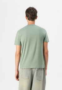 Tricou din bumbac verde, cu guler rotund și mâneci scurte, prezentat din spate. Croială lejeră, cu o textură netedă și un design minimalist.