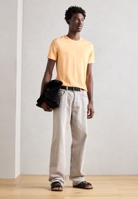 Tricou din bumbac portocaliu, blugi din denim gri, curea neagră, geantă neagră și sandale negre cu fâșii. Design minimalist, croială lejeră și textură ușoară.
