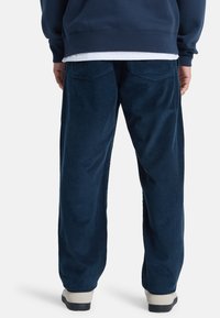 Marineblauwe corduroy broek met een relaxte pasvorm, voorzien van twee achterzakken en een gestructureerde stof, gecombineerd met lichtgekleurde schoeisel.