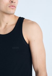 Schwarzes Tanktop mit Rundhalsausschnitt und minimalen Nähten. Besitzt ein dezentes "BOSS"-Logo auf der Vorderseite. Glatte Textur.