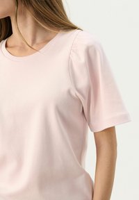 T-shirt rosa chiaro con collo rotondo e maniche corte a sbuffo. Realizzata in tessuto morbido, presenta un design semplice senza fantasie.