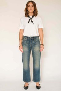 Jean en denim bleu taille haute avec jambes évasées, texture délavée, poches latérales et coutures contrastantes. Porté avec un t-shirt blanc et des ballerines noires.