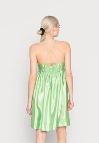 Vestido verde de cetim com um ajuste solto, costas franzidas e alças cruzadas. O tecido tem uma textura brilhante e cai acima do joelho.