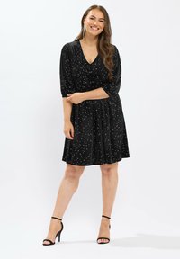 Schwarzes Kleid mit V-Ausschnitt, kurzen Puffärmeln, tailliertem Bund und einem fließenden Rock, der mit silbernen Punktmustern versehen ist.