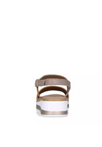 Sandalo marrone con sottili cinturini e suola piatta bianca, caratterizzato da un sottile dettaglio dorato e una singola cinghia alla caviglia regolabile. Texture in pelle liscia.