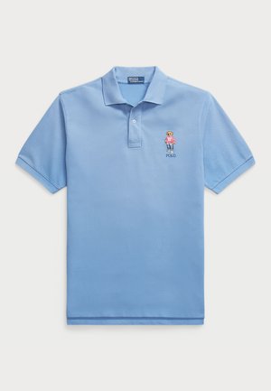 Polo azul claro feito de algodão, com uma pala de três botões e logótipo de urso bordado no lado esquerdo do peito. Mangas curtas.